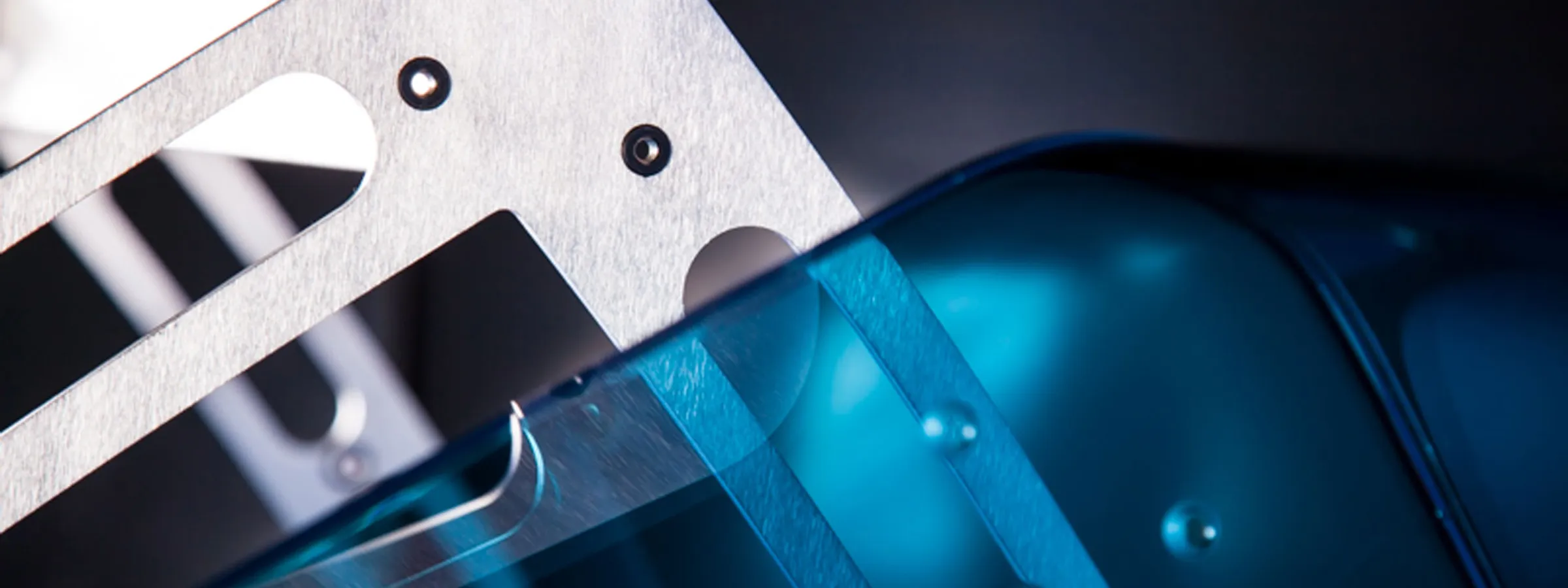 Gefräste Bauteile mit Langlöchern und Bohrungen neben einem blau transparenten Kunststoffteil